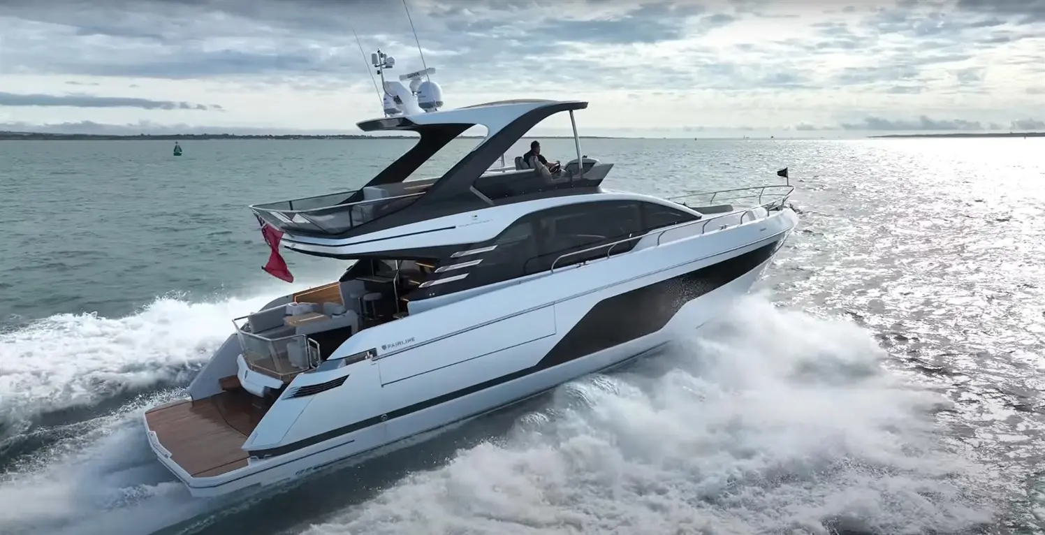 A sleek motor yacht navigates choppy waters, leaving a wake, with a man at the helm, under a cloudy sky.